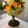 Round floral topiary in a white pot with yellow roses and orange blooms