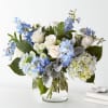 White roses and blue flowers arranged in a clear glass vase
