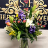 Mixed bouquet of lilies, roses, and purple flowers in a glass vase