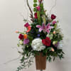 Tall mixed flower arrangement in a wooden vase with pink lilies and red roses