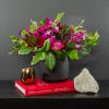 Pink and purple flower arrangement in a black vase with a gold candle and crystal.