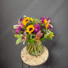 Mixed bouquet with sunflowers, lilies, and purple flowers in a glass vase