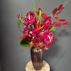 Tall tropical bouquet in a dark ribbed vase with red and pink blooms