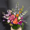 Colorful mixed bouquet in a green glass vase with roses, orchids, and purple blooms