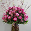Tall arrangement of pink roses with flowering branches in a clear glass vase on a wooden table