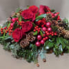 Low arrangement of red roses with red berries, pinecones, and red ornaments in a holiday centerpiece