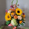 Tall mixed arrangement with sunflowers, hydrangea, and assorted orange and peach blooms in a glass vase.