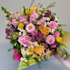 Hand-tied bouquet of pink and yellow flowers including roses, snapdragons, carnations, and daisies in bright wrap.