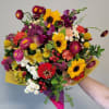 Hand-tied bouquet of bright sunflowers and mixed red and purple blooms wrapped in yellow and magenta paper