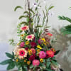Tall mixed arrangement of pink and orange blooms with yellow accents in a gold pedestal vase