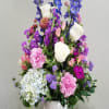 Tall mixed arrangement of purple, pink, blue, and white flowers in a white vase on a dark table