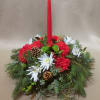 Low centerpiece of red carnations, white mums, evergreen branches and a tall red taper candle.