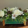 Low rectangular holiday arrangement with white flowers, pinecones, and evergreens in a green wooden box.