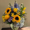 Arrangement of yellow sunflowers, roses, and blue hydrangeas in a clear glass vase