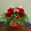 Low red holiday arrangement with red amaryllis, red carnations, evergreens, and pine cones in a snowflake container.
