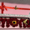Pink gift box with red roses arranged inside and a red ribbon on the lid