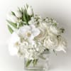 White roses, orchids, and tulips arranged in a clear square vase