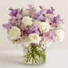 White roses and pink-purple flowers arranged in a clear glass vase