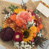 Mixed bouquet with orange roses, sunflowers, and pink carnations in brown paper