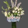 Tall bouquet of white roses, blue hydrangeas, and pale orchids in a glass vase