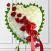 Heart-shaped white floral arrangement with red roses and a red ribbon