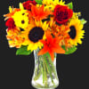 Bouquet of sunflowers, red roses, and orange lilies in a clear glass vase
