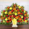 Large colorful floral spray with orange lilies and roses in a white pedestal vase
