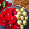 Red roses and gold-wrapped chocolates arranged on a black round box with a card.