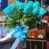 Blue roses in a glass vase with a ribbon and chocolates in a gift bag