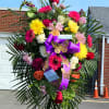 Large standing floral spray with bright mixed flowers and purple ribbon
