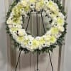 White floral wreath on a black stand with roses and mums