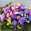 Large floral arrangement with purple hydrangeas, pink carnations, and a purple ribbon