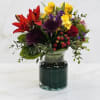 Bright mixed bouquet with red lilies, yellow blooms, purple mums and red roses in a clear glass vase