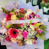 Large bouquet of pink, white, and peach flowers wrapped in lavender paper