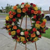 Large floral wreath on a wooden stand with orange, red, yellow, and white blooms