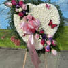 Heart-shaped white floral spray with pink and purple roses and ribbon