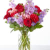 Bouquet of red roses and purple flowers in a clear glass vase