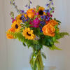 Bouquet of orange roses, sunflowers, and blue flowers in a glass vase