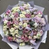 Large pastel bouquet of roses and white blooms wrapped in lavender paper