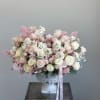 Large pastel bouquet of roses and white filler flowers in a white urn vase