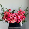 Large pink floral arrangement in a black container with ribbon
