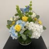 Blue and white hydrangeas with yellow roses in a glass vase
