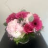 Pink gerbera daisies, a rose, and pale hydrangea in a glass vase