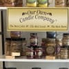 Shelf display of scented candles in mason jars with a company sign.