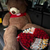 A large, luxurious teddy bear holding a beautifully designed box filled with