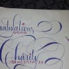 Decorative calligraphy reading "Congratulations Grad" and a name on white paper