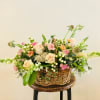 Basket arrangement of pale roses and pink flowers with greenery
