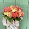 Pink and peach roses in a wrapped bouquet with a ribbon tag