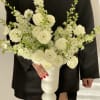 White floral arrangement in a white pedestal vase held against a black outfit