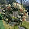 Large floral wreath of white and peach flowers on a stand outdoors